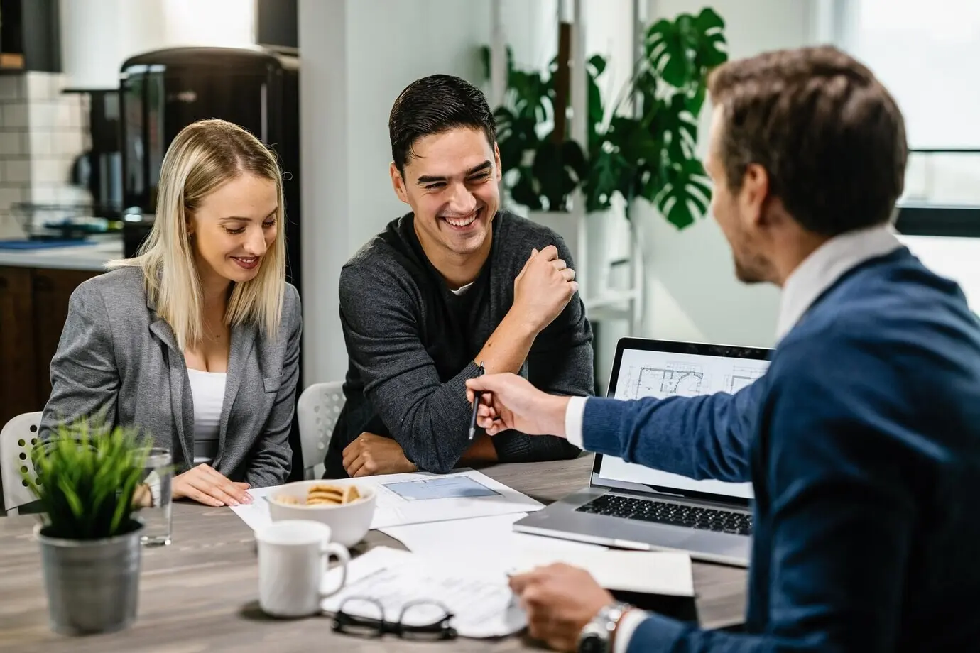 A happy couple meets with a real estate agent, analyzing blueprints as they talk.