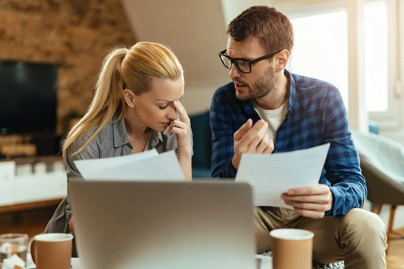 A young couple, looking displeased, converse while analyzing their home finances.